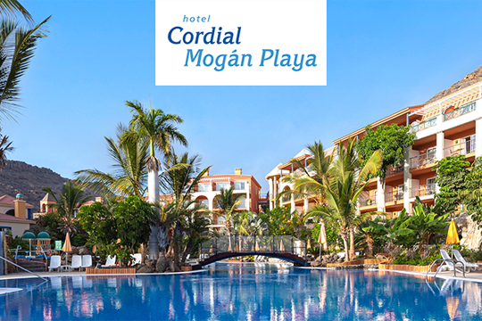 Blick &uuml;ber Hotelanlage mit roten Geb&auml;uden, unten am Bild und in der Mitte Pools zu sehen, am Horizont eine Gebirgskette